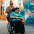 Woman support working pushing an individual in a wheelchair in front of a colorful graffiti wall