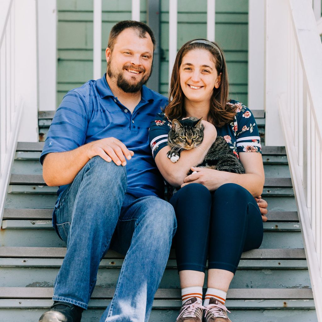 Two self-advocates sitting on a staircase outside snuggling with a cat