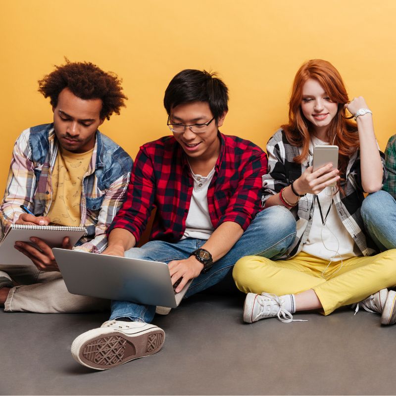 Three youth sitting on the ground looking at their various digital devices