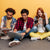 Three youth sitting on the ground looking at their various digital devices